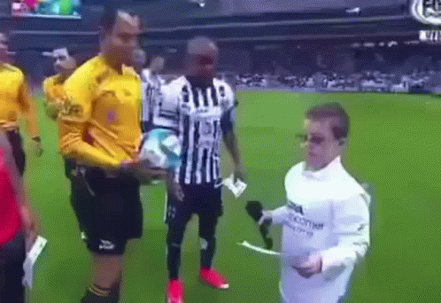 A Man In A White Shirt Is Holding A Microphone And Talking To A Soccer Player On A Field . GIF