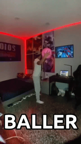 A Man In A White Shirt Is Holding A Pink Ball In A Living Room With The Word Baller On The Floor GIF