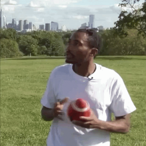 A Man In A White Shirt Is Holding A Red Ball In His Hands GIF