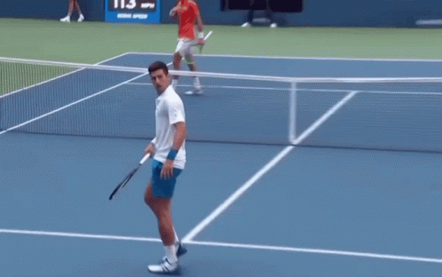 A Man In A White Shirt Is Holding A Tennis Racquet GIF