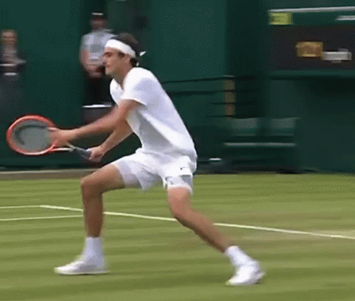 A Man In A White Shirt Is Holding A Tennis Racquet On A Court GIF