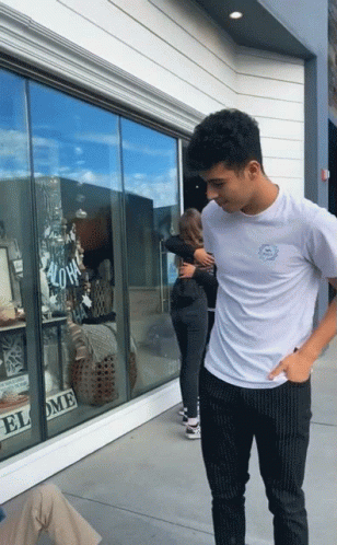 A Man In A White Shirt Is Hugging A Woman In Front Of A Store Window That Says " Aloha " GIF