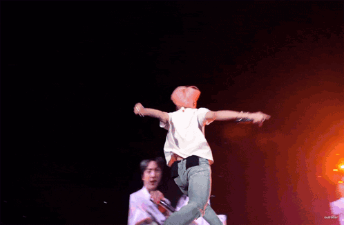 A Man In A White Shirt Is Jumping In The Air On A Stage GIF