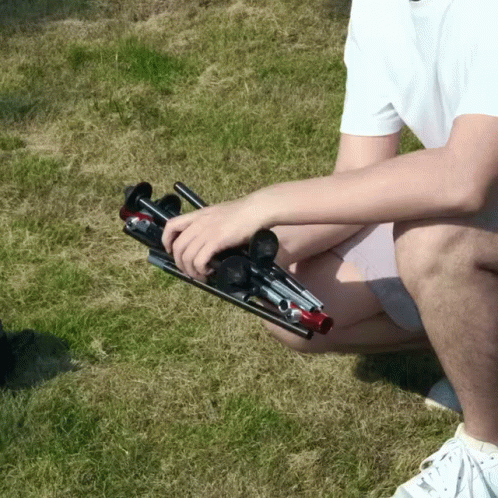 A Man In A White Shirt Is Kneeling Down In The Grass Holding A Folding Stool GIF