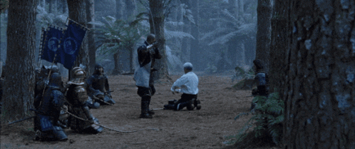 A Man In A White Shirt Is Kneeling Down Next To A Man In Armor With A Sword GIF