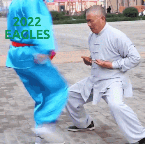 A Man In A White Shirt Is Kneeling Down Next To Another Man In A Blue Shirt With 2022 Eagles Written On The Top GIF