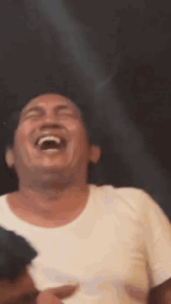 A Man In A White Shirt Is Laughing With His Mouth Open And His Eyes Closed . GIF