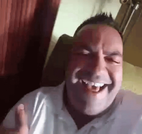 a man in a white shirt is laughing with his mouth open while sitting in a chair .