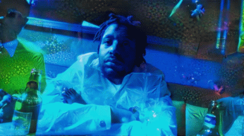 A Man In A White Shirt Is Laying On A Bed With A Bottle Of Beer GIF