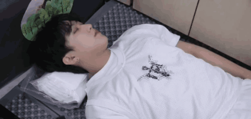 A Man In A White Shirt Is Laying On The Floor With A Pillow . GIF