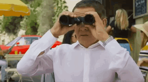 a man in a white shirt is looking through binoculars in a crowded street .
