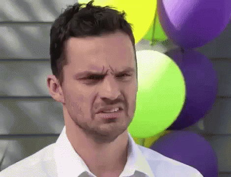 A Man In A White Shirt Is Making A Funny Face While Standing In Front Of Balloons . GIF