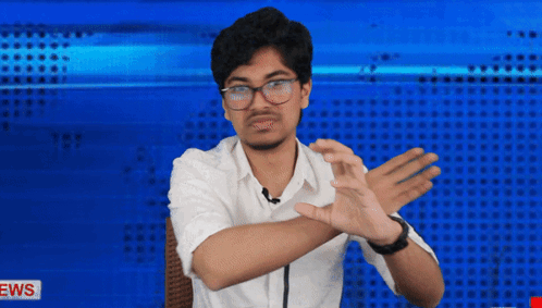 A Man In A White Shirt Is Making A Gesture With His Hands In Front Of A News Background GIF