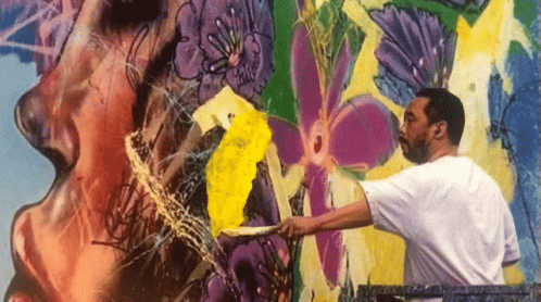 A Man In A White Shirt Is Painting A Colorful Mural On A Wall GIF