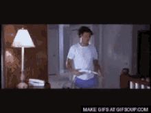 A Man In A White Shirt Is Playing A Video Game In A Dark Room . GIF
