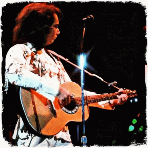 A Man In A White Shirt Is Playing An Acoustic Guitar In Front Of A Microphone GIF