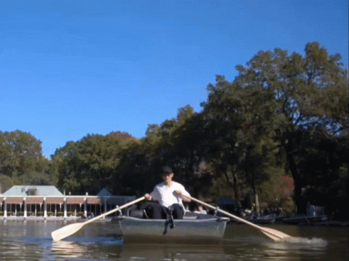 A Man In A White Shirt Is Rowing A Boat In A Lake GIF