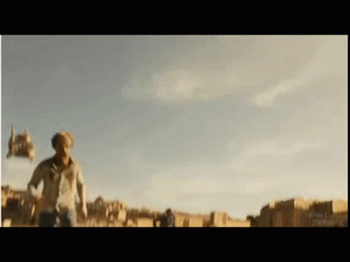 A Man In A White Shirt Is Running In A Field With A Blue Sky Behind Him GIF
