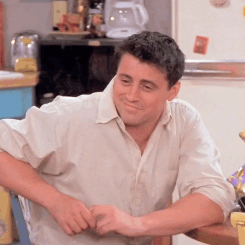 A Man In A White Shirt Is Sitting At A Table GIF