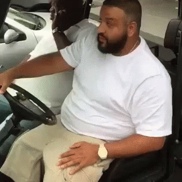 A Man In A White Shirt Is Sitting In A Car Holding The Steering Wheel . GIF