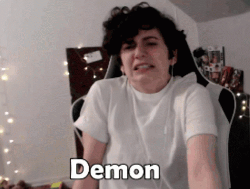 A Man In A White Shirt Is Sitting In A Chair And The Word Demon Is On His Chest GIF