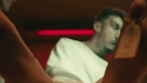 A Man In A White Shirt Is Sitting In A Chair In A Dark Room With His Legs Crossed . GIF
