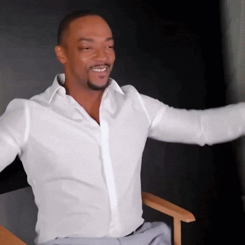 A Man In A White Shirt Is Sitting In A Chair With His Arms Outstretched And Smiling GIF