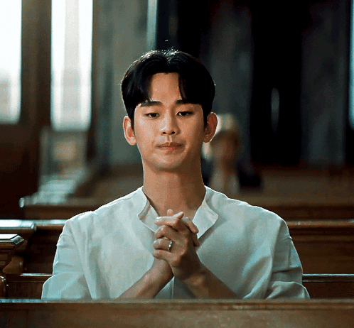 A Man In A White Shirt Is Sitting In A Church With His Hands Folded GIF