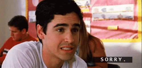 A Man In A White Shirt Is Sitting In A Classroom And Making A Face . GIF