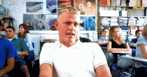 A Man In A White Shirt Is Sitting In A Classroom With A Group Of Students . GIF