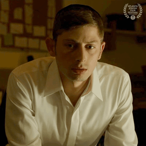 Man In White Shirt Sitting In Front Of Laurel Wreath GIF