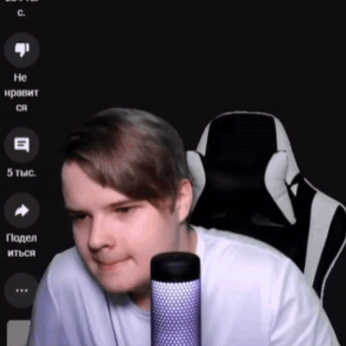 A Man In A White Shirt Is Sitting In Front Of A Microphone With A Black And White Chair Behind Him GIF