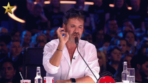 A Man In A White Shirt Is Sitting In Front Of A Microphone With A Gold Star Above Him GIF