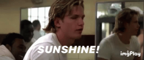 A Man In A White Shirt Is Sitting In Front Of A Mirror With The Words Sunshine Written On It . GIF