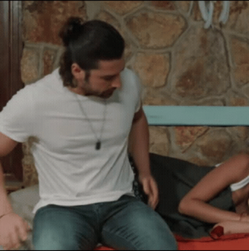 A Man In A White Shirt Is Sitting On A Bed GIF