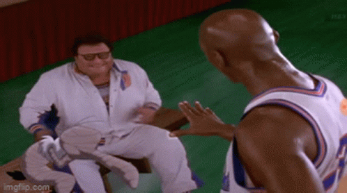 A Man In A White Shirt Is Sitting On A Bench Talking To Another Man In A Basketball Uniform . GIF