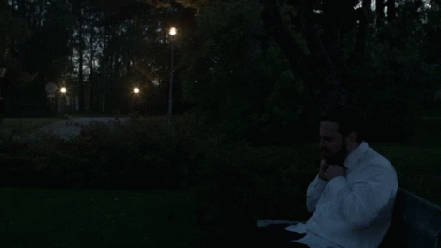 A Man In A White Shirt Is Sitting On A Park Bench GIF