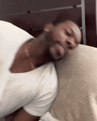A Man In A White Shirt Is Sleeping On A Bed With His Head On A Pillow GIF