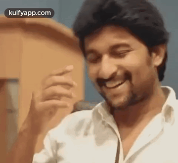 A Man In A White Shirt Is Smiling And Laughing While Standing In Front Of A Microphone . GIF