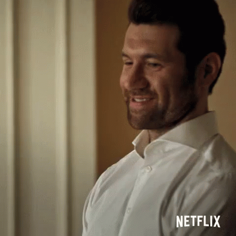 A Man In A White Shirt Is Smiling And Looking At Something . GIF