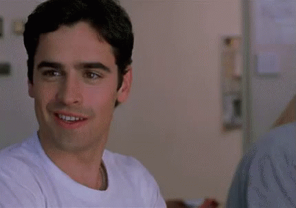 A Man In A White Shirt Is Smiling In A Room . GIF