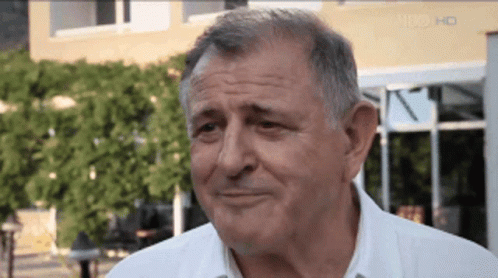 A Man In A White Shirt Is Smiling In Front Of A Building That Says Hd On The Bottom GIF