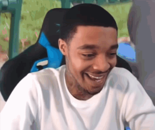 A Man In A White Shirt Is Smiling While Sitting In A Gaming Chair . GIF