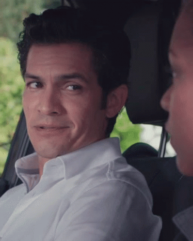 A Man In A White Shirt Is Smiling While Sitting In The Back Seat Of A Car GIF