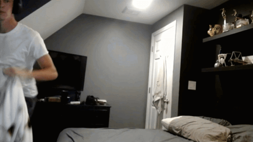 A Man In A White Shirt Is Standing In A Bedroom GIF
