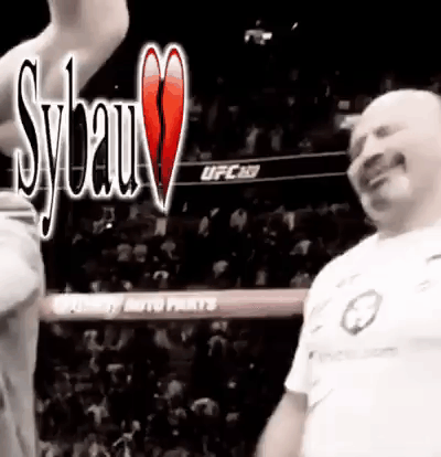 A Man In A White Shirt Is Standing In A Boxing Ring With A Crowd In The Background . GIF