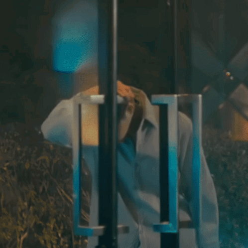 A Man In A White Shirt Is Standing In A Dark Room With His Head Down GIF