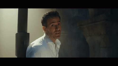 A Man In A White Shirt Is Standing In A Dark Room With His Mouth Open GIF