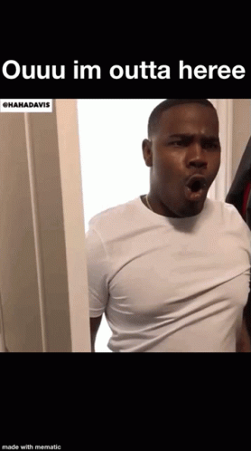 A Man In A White Shirt Is Standing In A Doorway . GIF