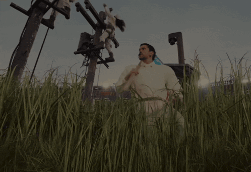A Man In A White Shirt Is Standing In A Field With A Stadium In The Background GIF